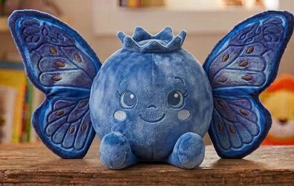 The Blueberry colourway — a round plush with embroidered wings, sitting on a wooden shelf